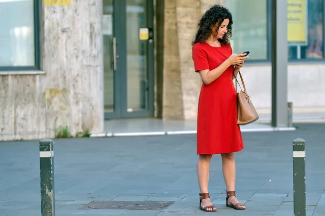 woman, red dress, phone, purse, bag, young, building, urban, town, person, sidewalk, snapshot, street photography, looking, smartphone, standing, pavement, waiting. How to make sound decisions about a social media feed