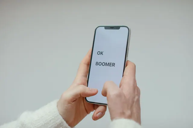 Close-up of a person holding a smartphone displaying 'OK Boomer' against a plain background. Meme culture: a practical guide to meaning, context, and sharing