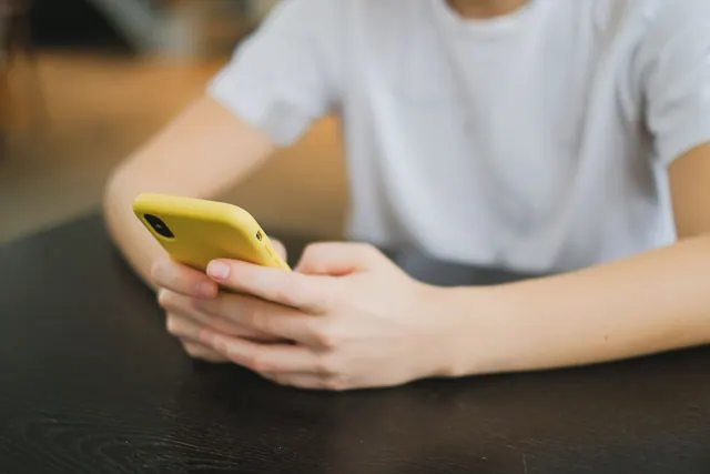 Close-up of person holding a yellow smartphone indoors, focused on the hands and gadget. Meme formats compared by meaning, effort, and context