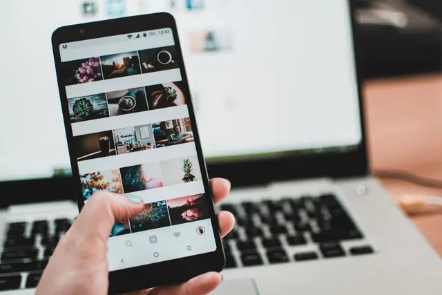 A person uses a smartphone to browse social media in front of a laptop, emphasizing modern technology and lifestyle. Social media feeds: a practical guide to reading them well