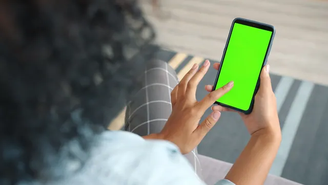 A person interacts with a smartphone displaying a green screen, ideal for mockups. A pass-or-review checklist for social media feeds