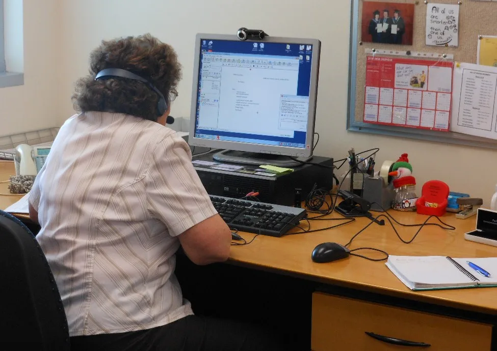 A person wearing a headset while using a desktop computer for an online meeting