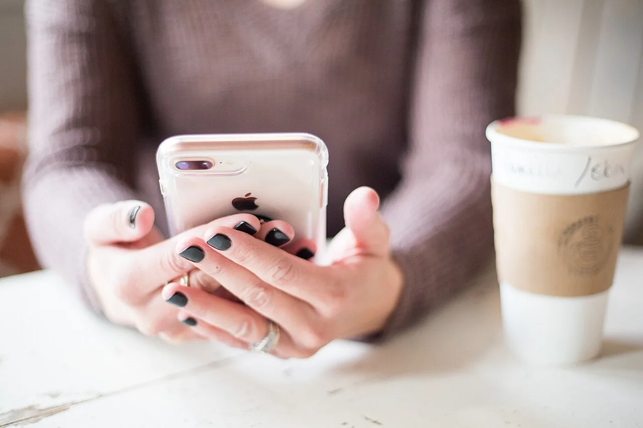 Close view of a person holding and using a smartphone beside a cup